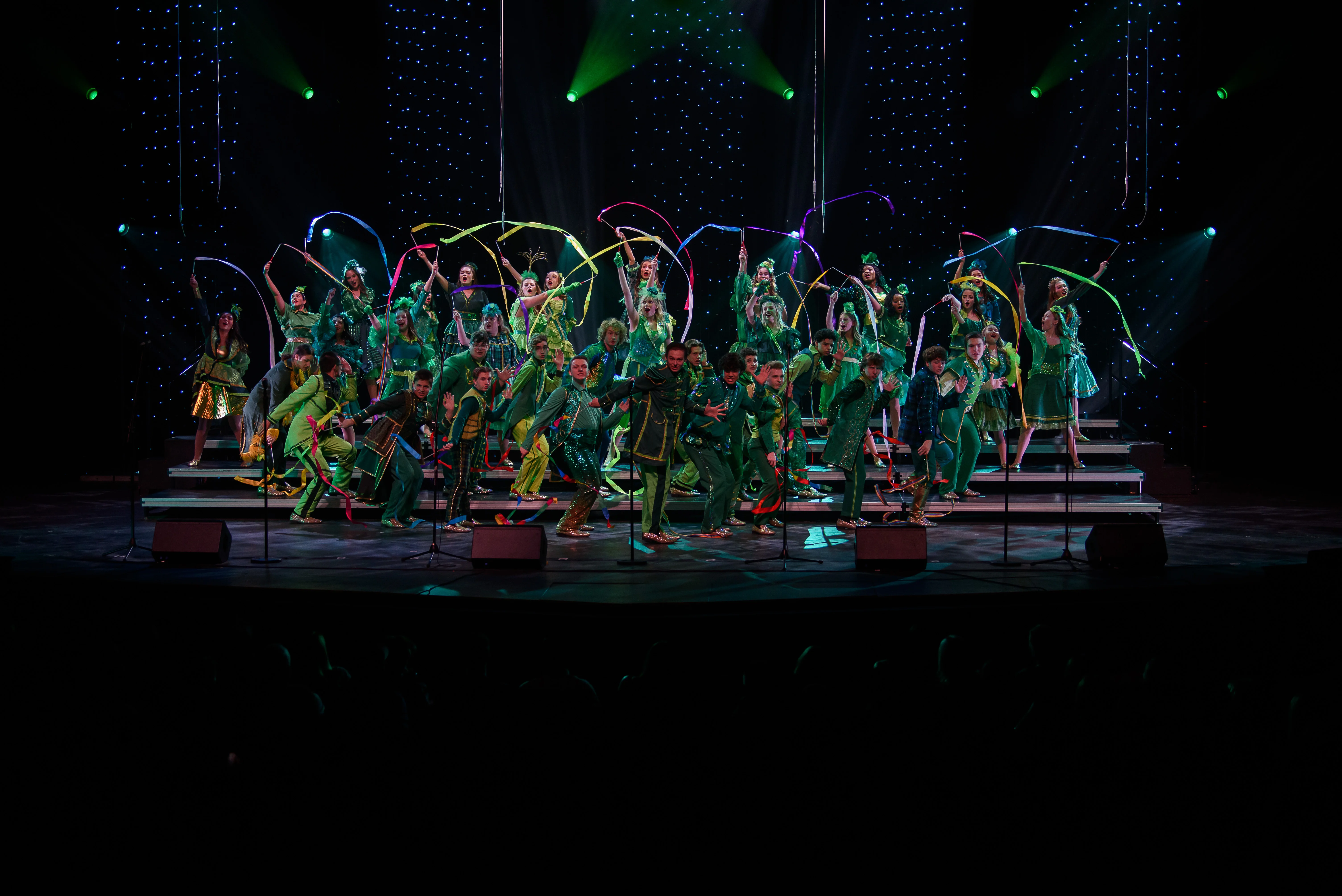 Choir performers on a lit stage with microphones across the front