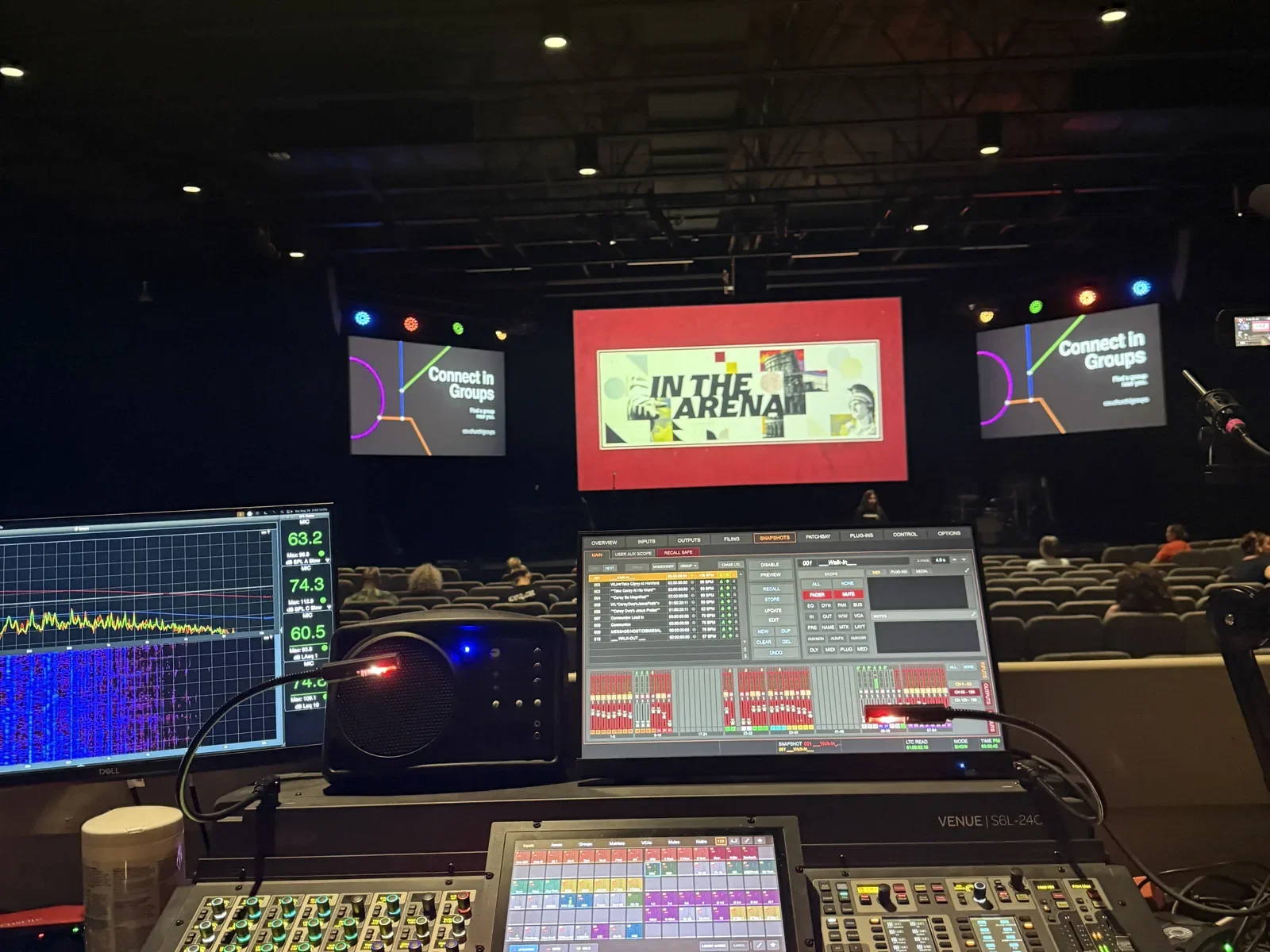 Production control desk facing a lit auditorium stage and presentation screens